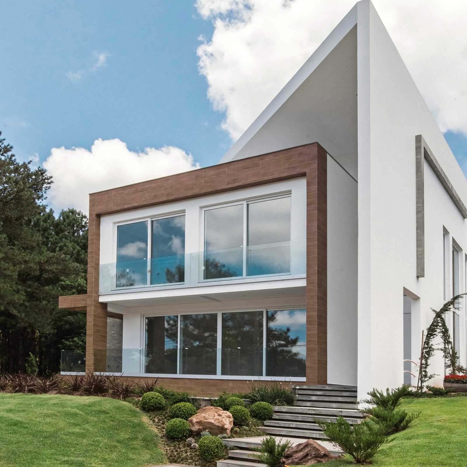 Een modern huis met twee verdiepingen en grote ramen, omgeven door een goed onderhouden tuin en bloeiende vegetatie.
